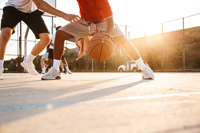 Un homme en short gris et chemise rouge dribble un ballon de basket.