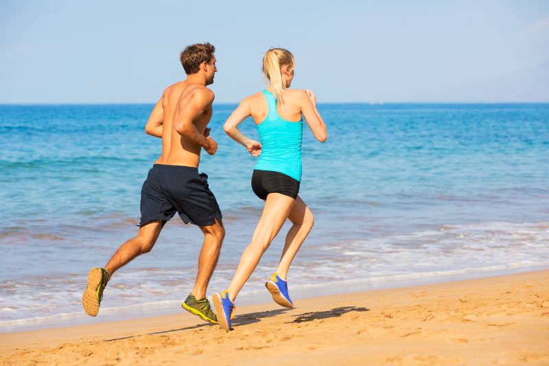 Couple en cours d'exécution.  Coureurs sportifs faisant du jogging sur la plage travaillant en souriant heureux.  Concept d'exercice de remise en forme.