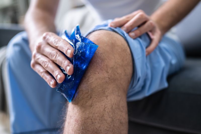 Gros plan d'une personne assise et appliquant un pack de gel de glace sur un genou blessé