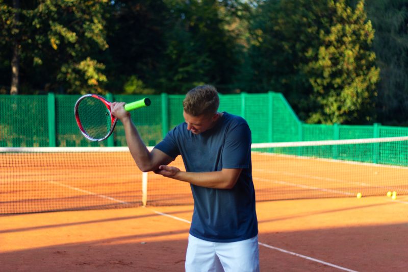 Bel homme sur un court de tennis.  Jeune joueur de tennis.  Douleur au coude