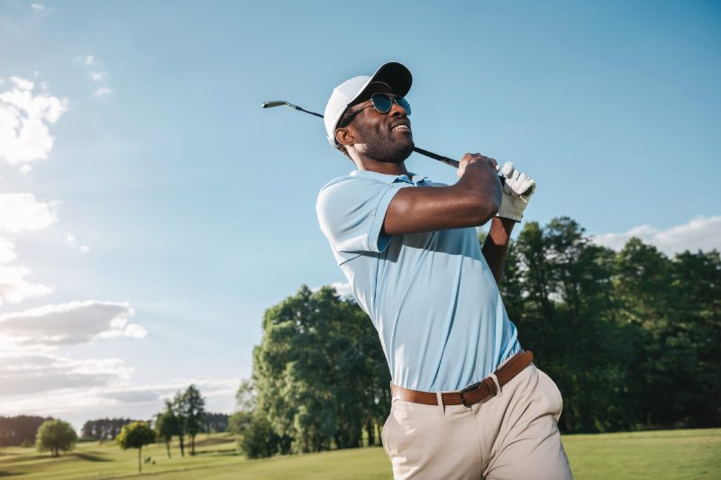 Homme afro-américain souriant en casquette et lunettes de soleil jouant au golf