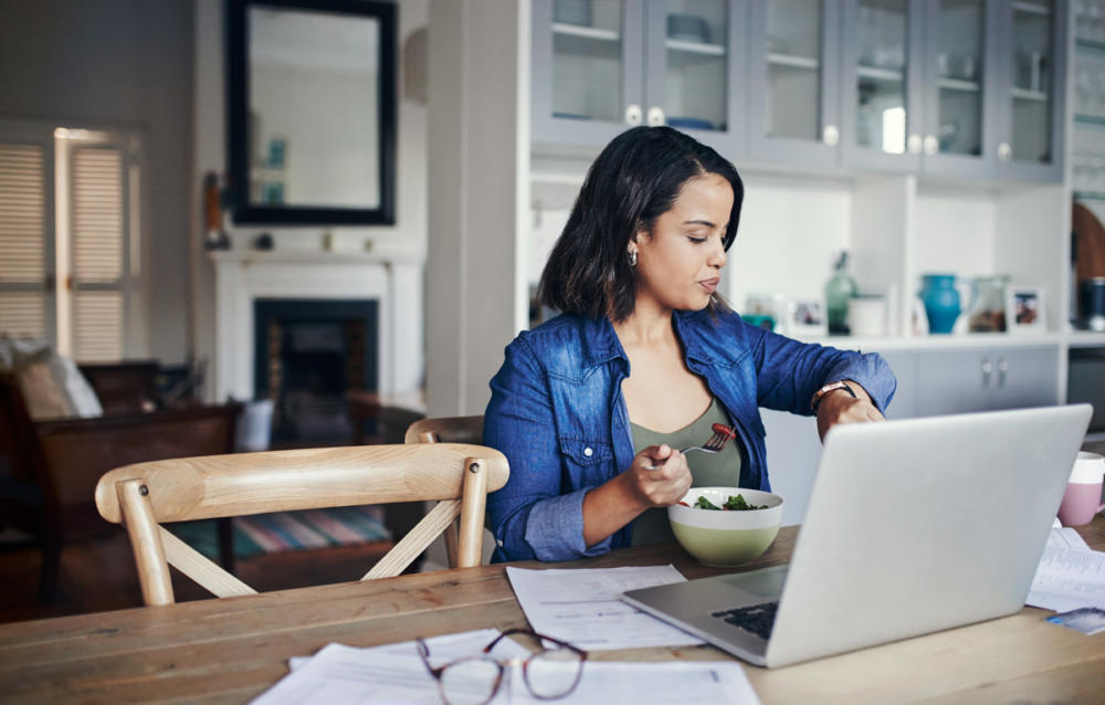 Femme mangeant à la table de la cuisine tout en travaillant sur ordinateur