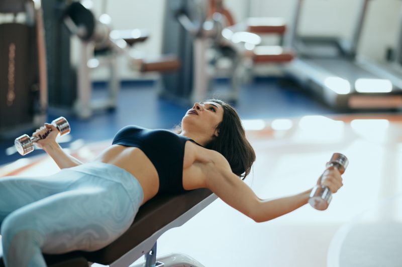 Une jolie femme bodybuilder soulève des haltères en s'allongeant sur le banc de la salle de sport.